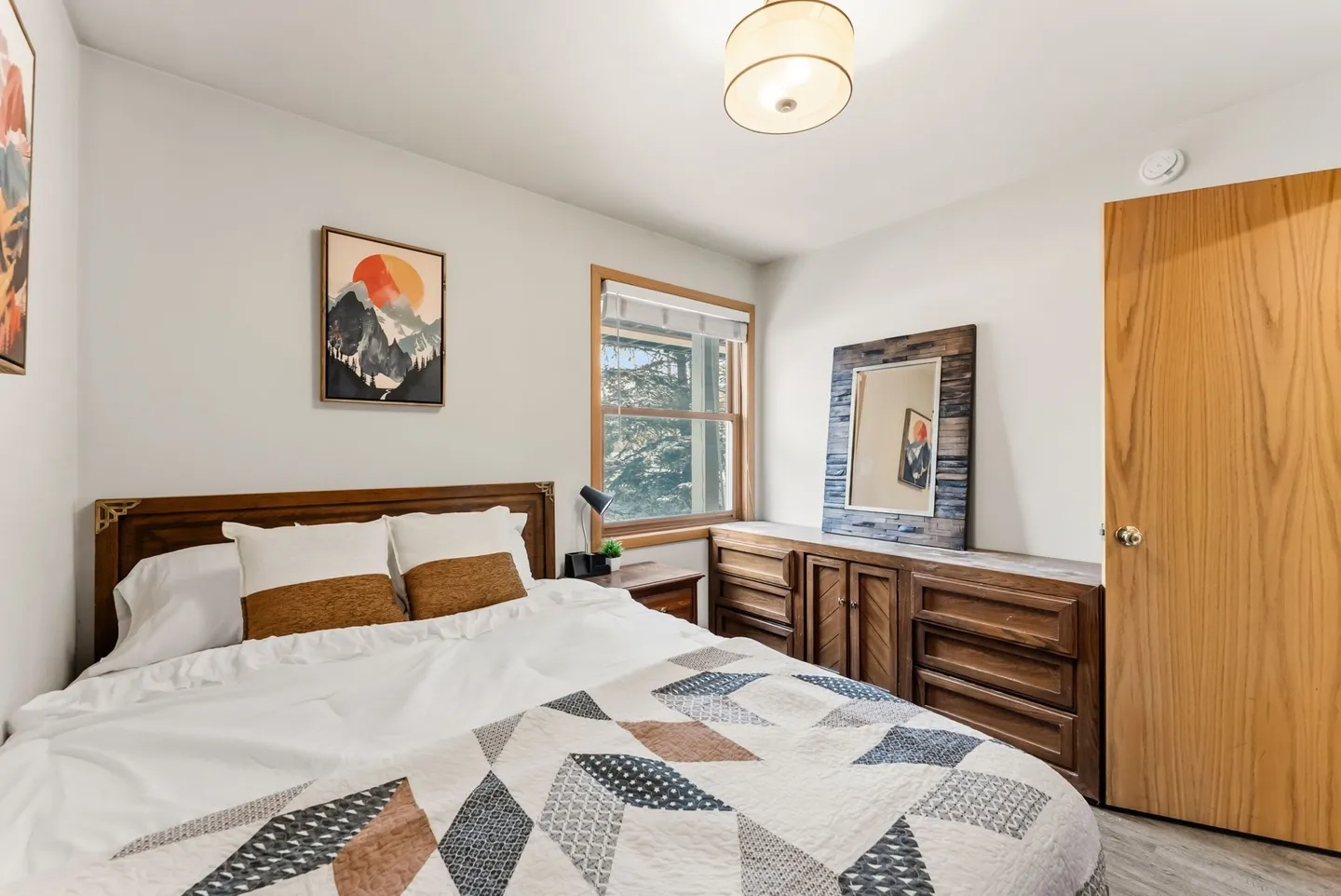 Bedroom featuring a made bed with a patterned quilt, wooden headboard, matching wooden dresser, and a window with blinds.
