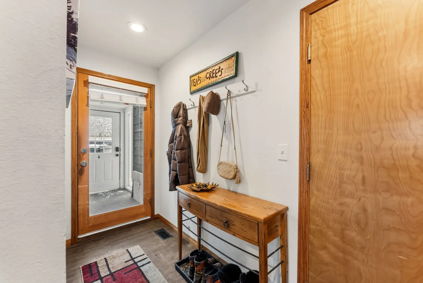 Entryway with a glass paneled front door, wooden console table, wall coat hooks, and an interior wooden door.