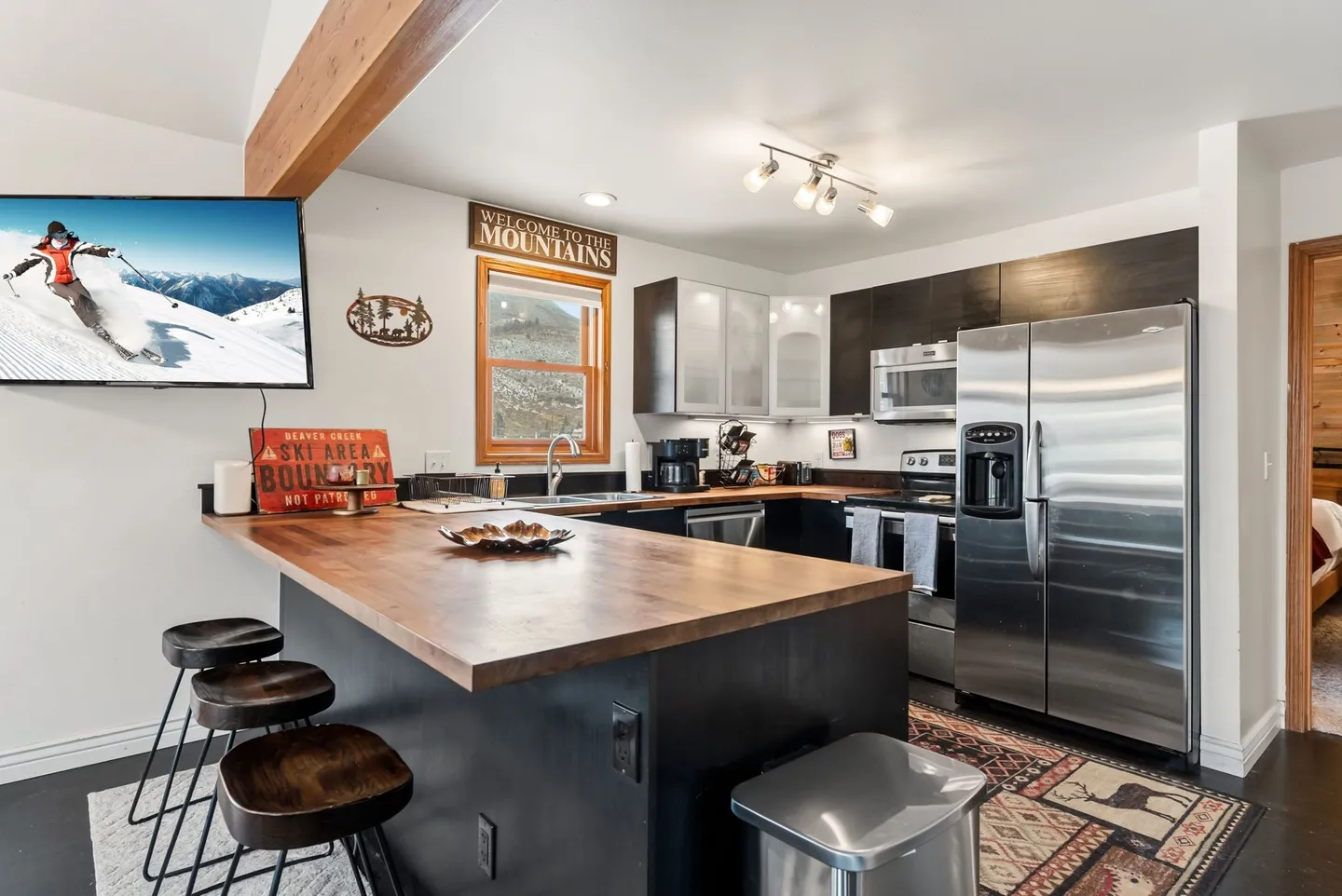 Kitchen featuring a wood-topped breakfast bar with three stools, stainless steel appliances, and a wall-mounted TV.
