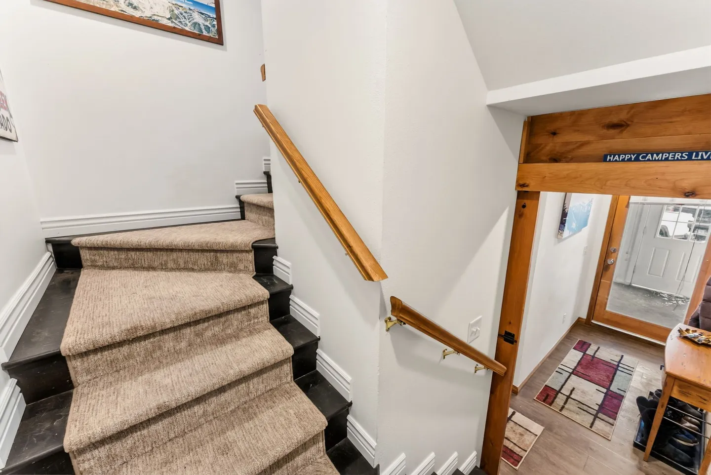 A carpeted staircase with a wooden handrail looking down toward a home entrance.
