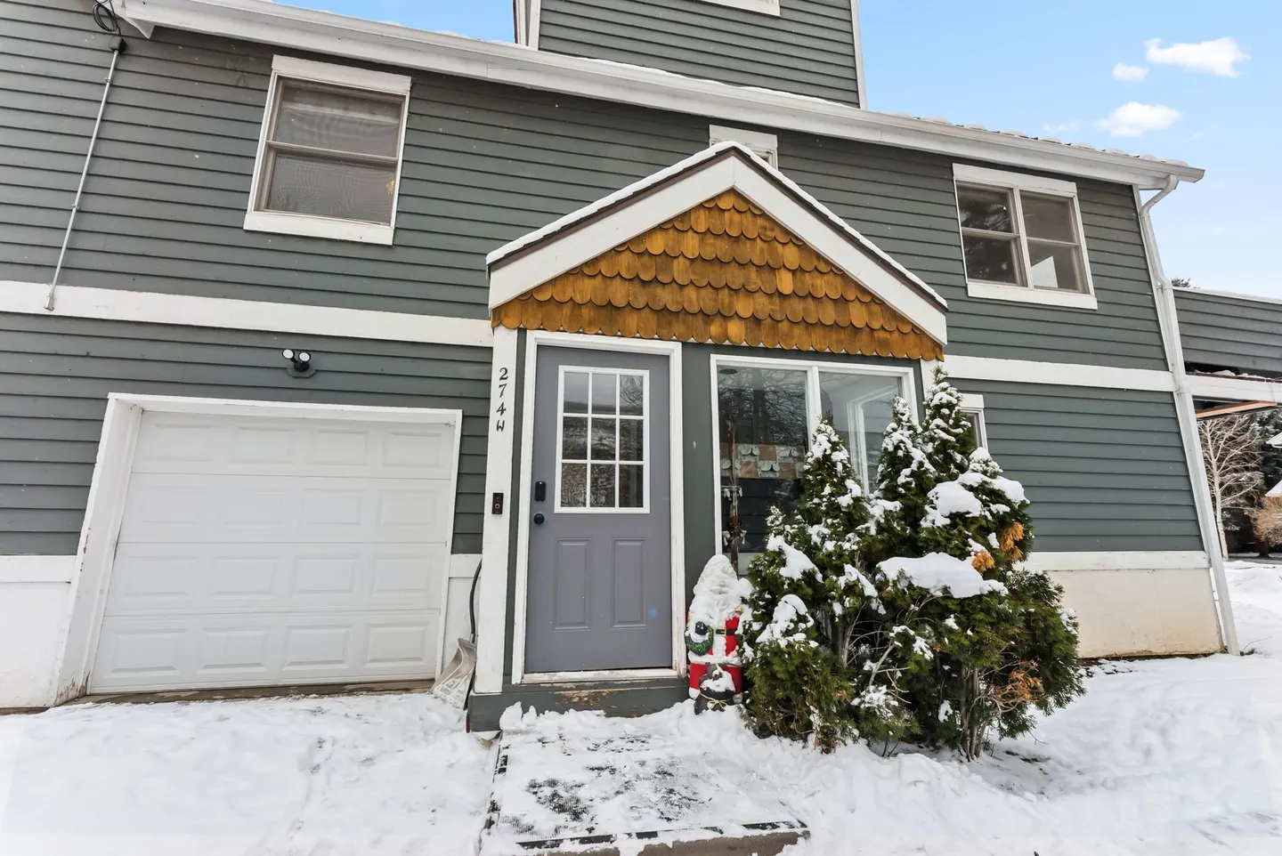 Exterior front entryway of a townhouse in winter with blue-gray siding, a garage door, and snow on the ground.