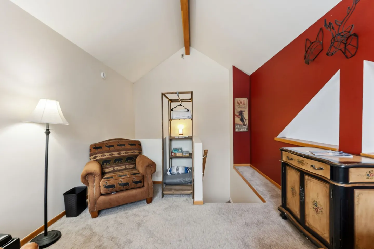 Upstairs landing with carpet, an armchair, standing lamp, storage rack, painted cabinet, and red accent wall.