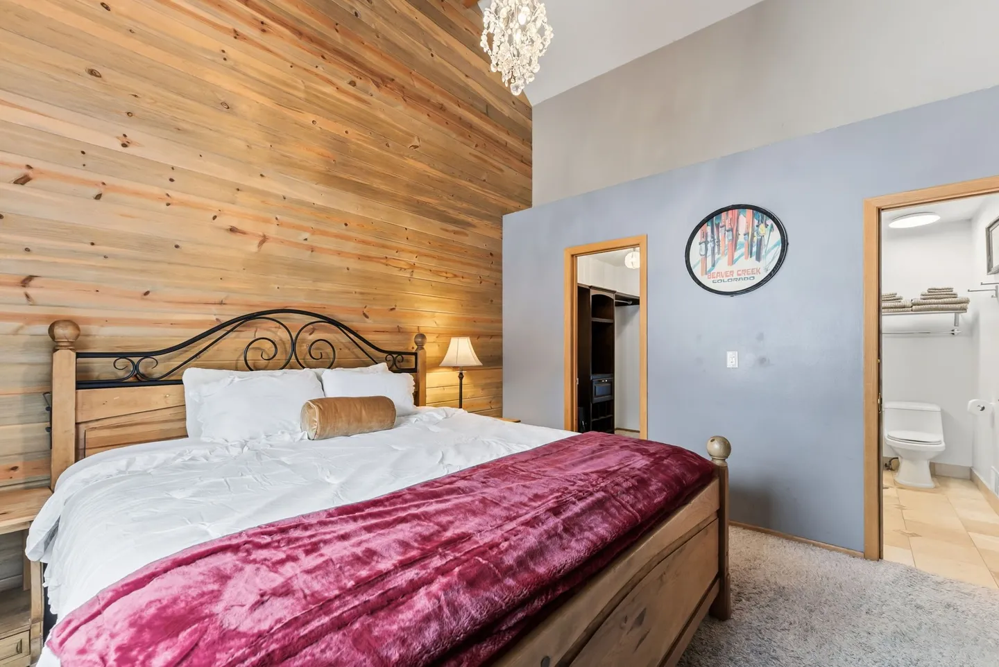 Bedroom featuring a wood-plank accent wall behind a bed, a vaulted ceiling with a chandelier, and doorways leading to a closet and an en suite bathroom.