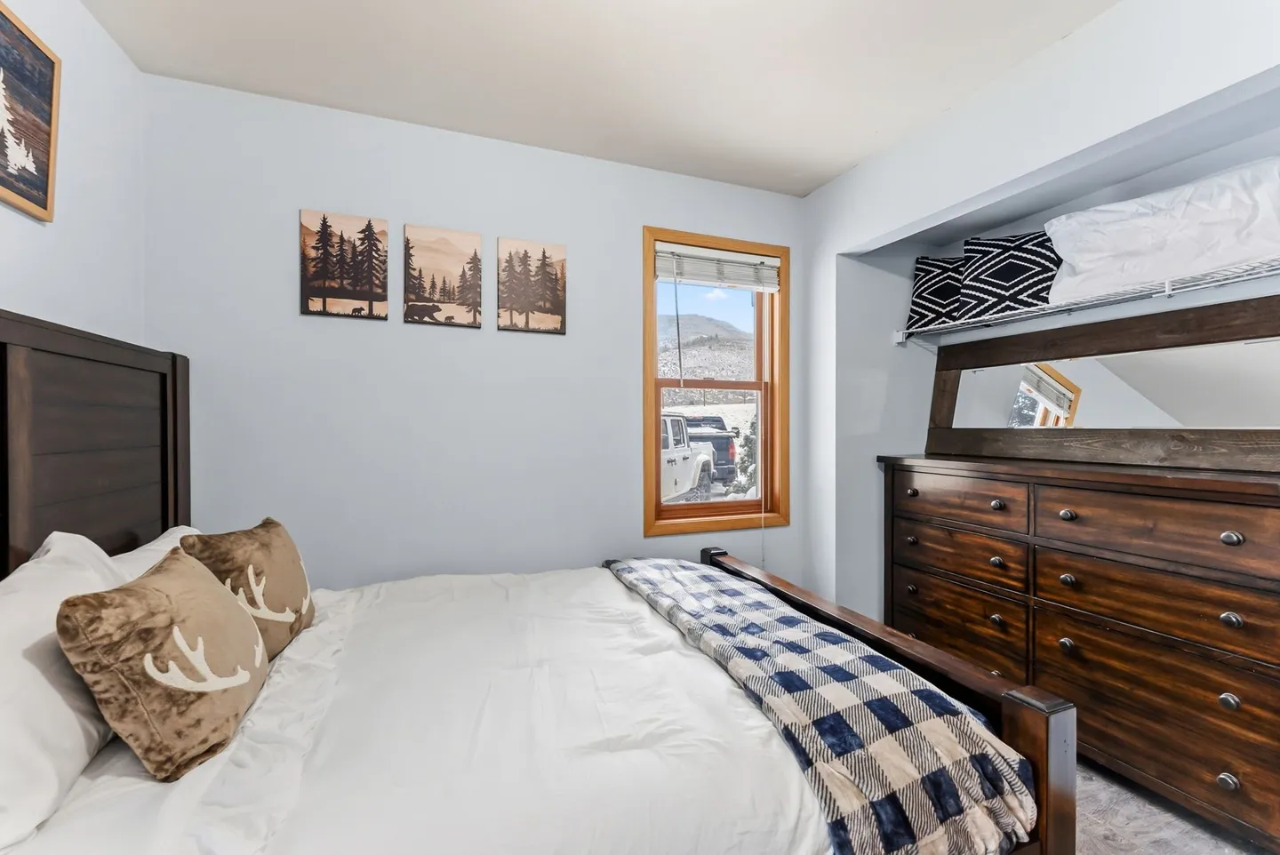 Bedroom with a wooden bed, light blue walls, a dark wood dresser tucked into a closet nook, and a window with mountain views.