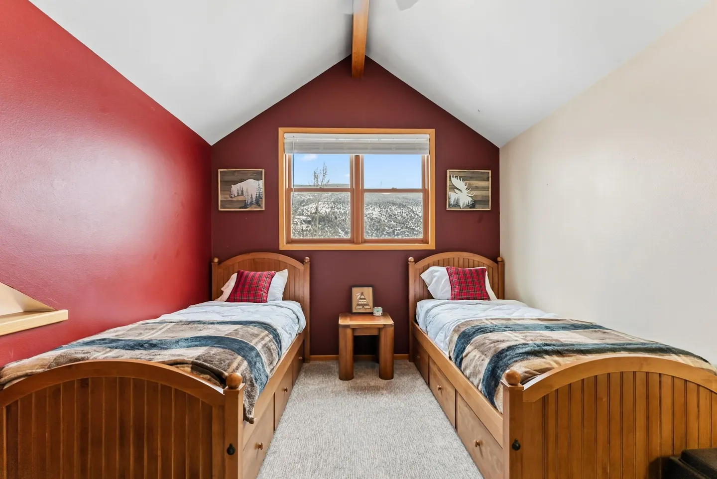 Bedroom featuring vaulted ceilings, a red accent wall, a center window, and two matching wooden twin beds with plaid bedding.