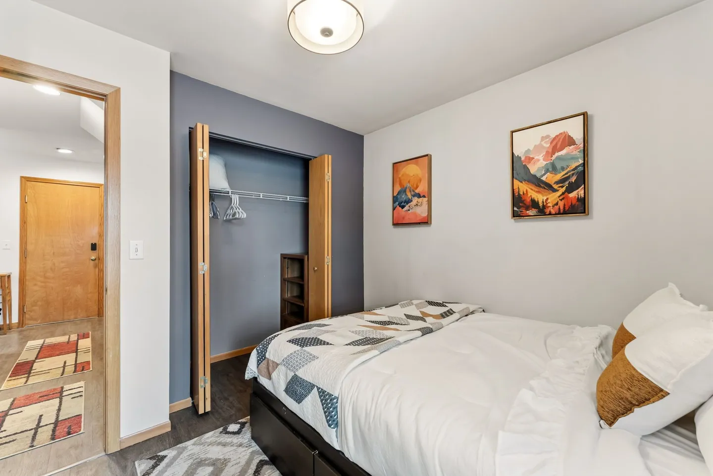 Bedroom with a made bed, open bi-fold closet, framed wall art, and an open doorway leading to a hallway.