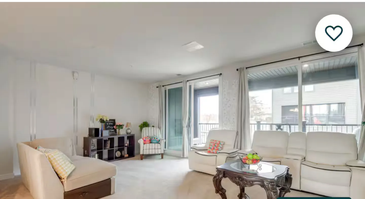 Living room with light-colored carpeting, multiple armchairs, a reclining sofa, and sliding glass doors leading outside.