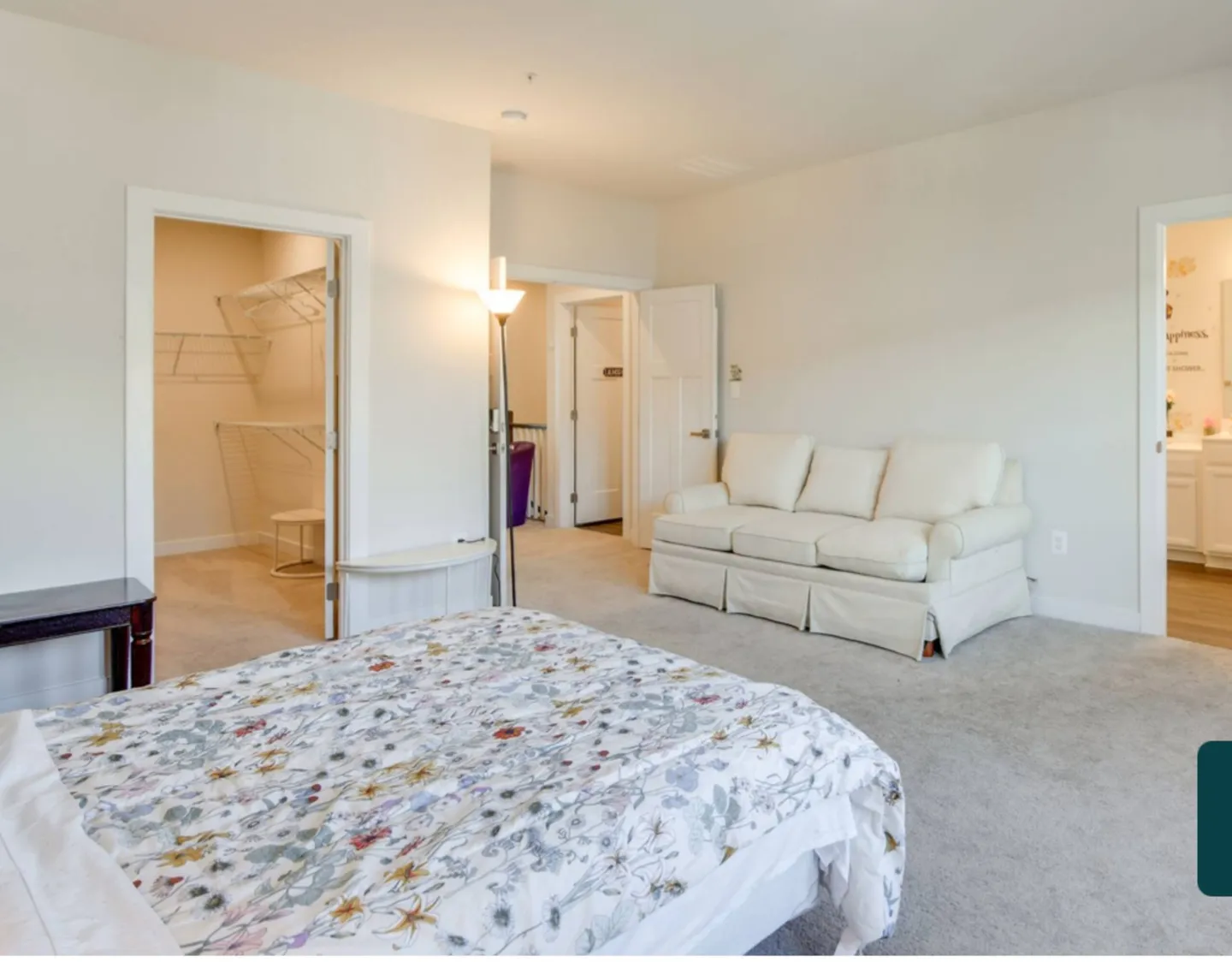 Bedroom featuring a floral bedspread, a cream-colored couch, carpeted flooring, and an open walk-in closet.