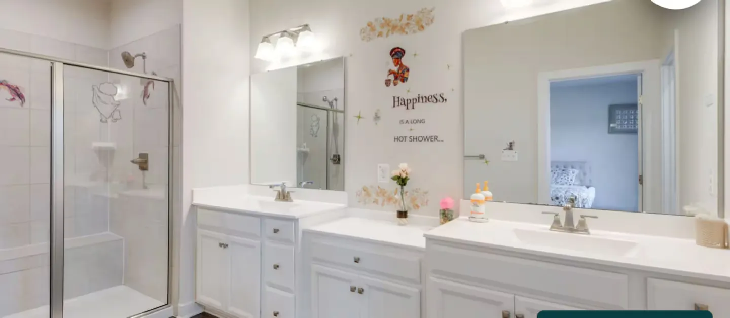 Bathroom with a double white vanity, mirrors, and a glass-enclosed walk-in shower with tiled walls.