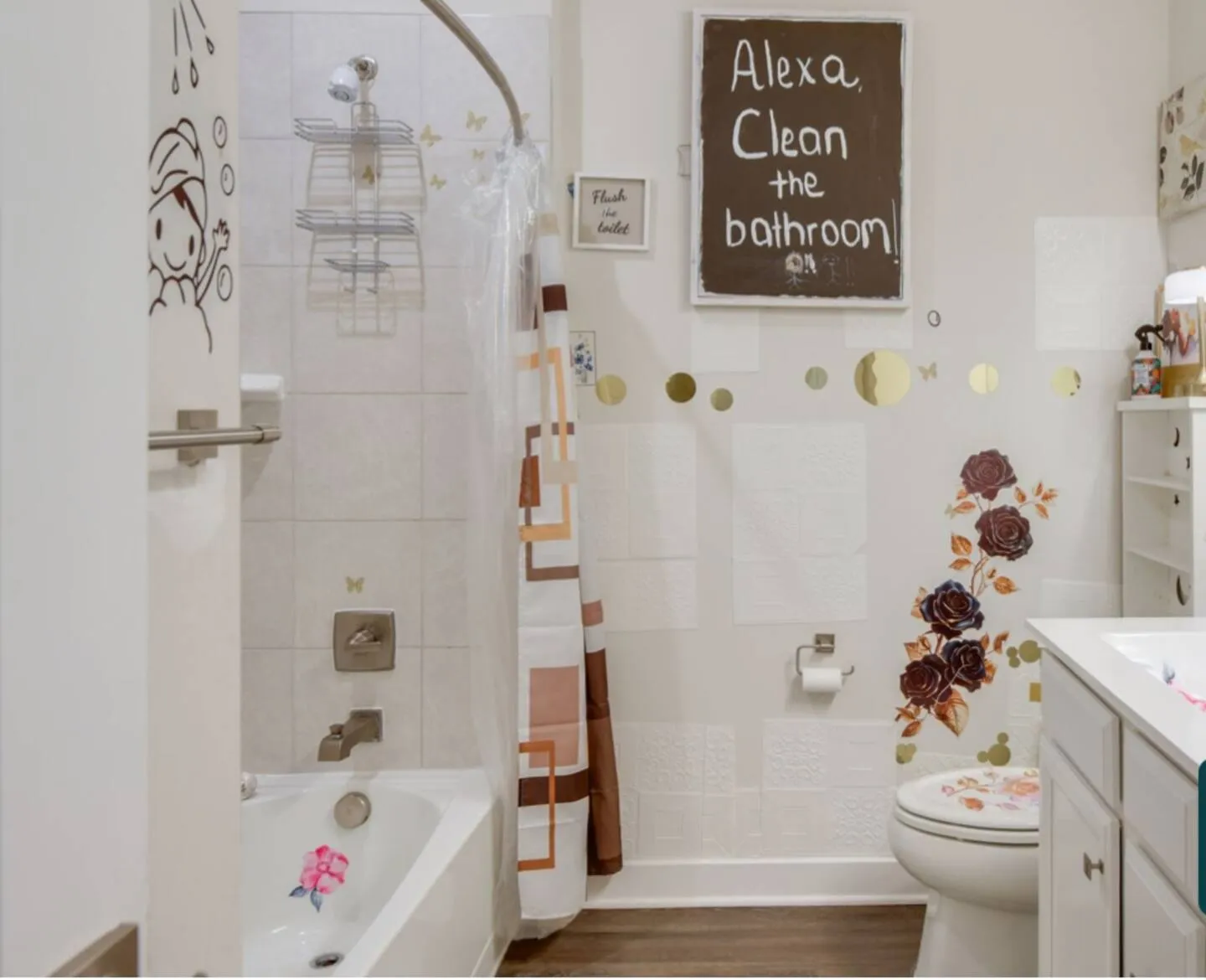 Bathroom with a bathtub shower combination, white toilet, and white vanity, featuring novelty wall signs and floral decals.