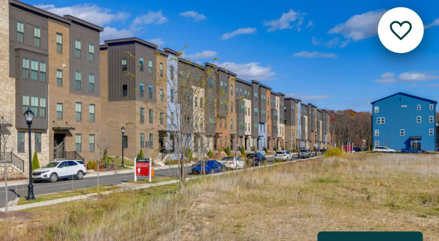 Exterior view of modern multi-story townhouses along a paved street under a bright blue sky.