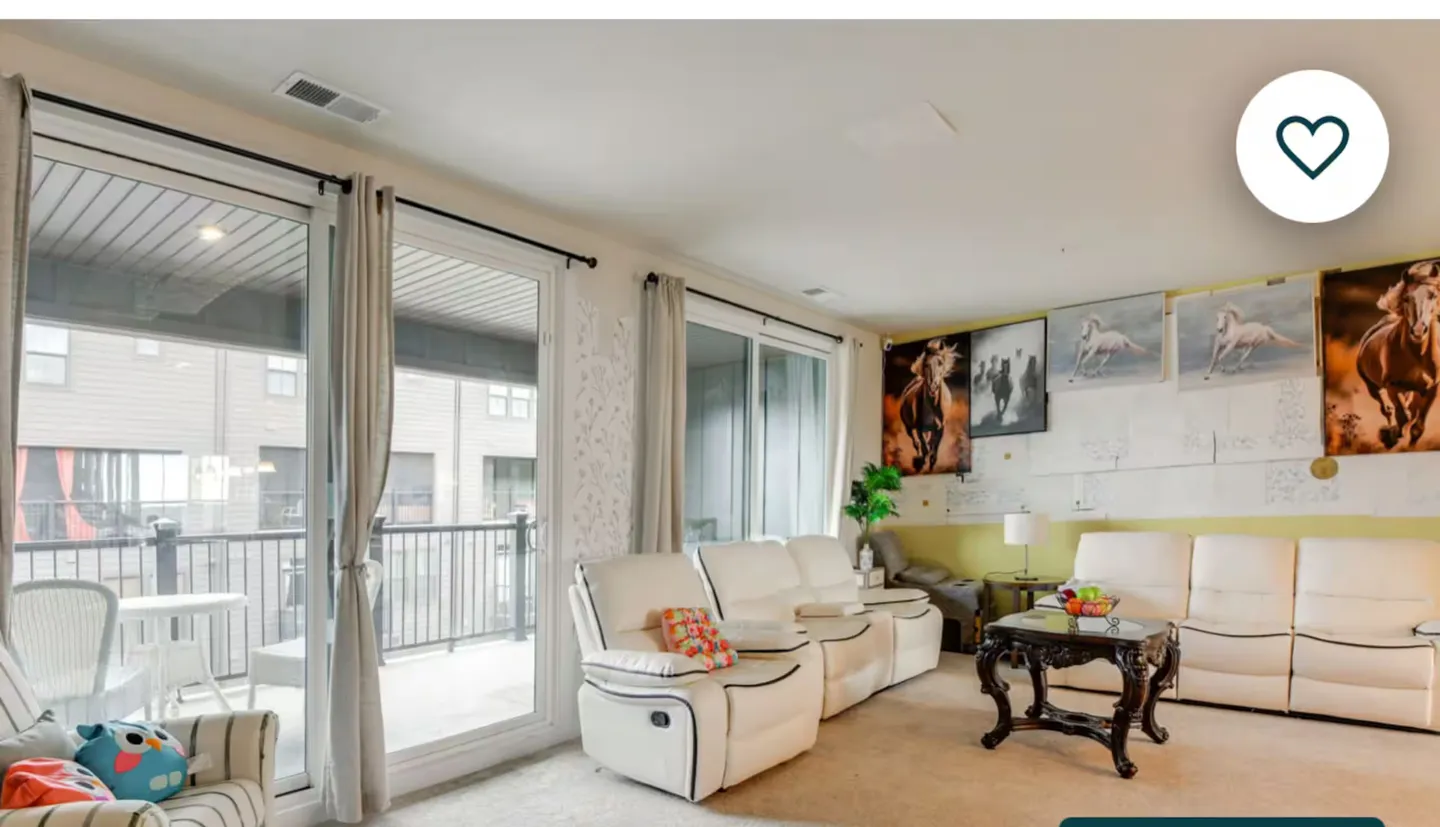Living room featuring reclining white sofas, a dark coffee table, sliding glass doors to a balcony, and horse wall art.
