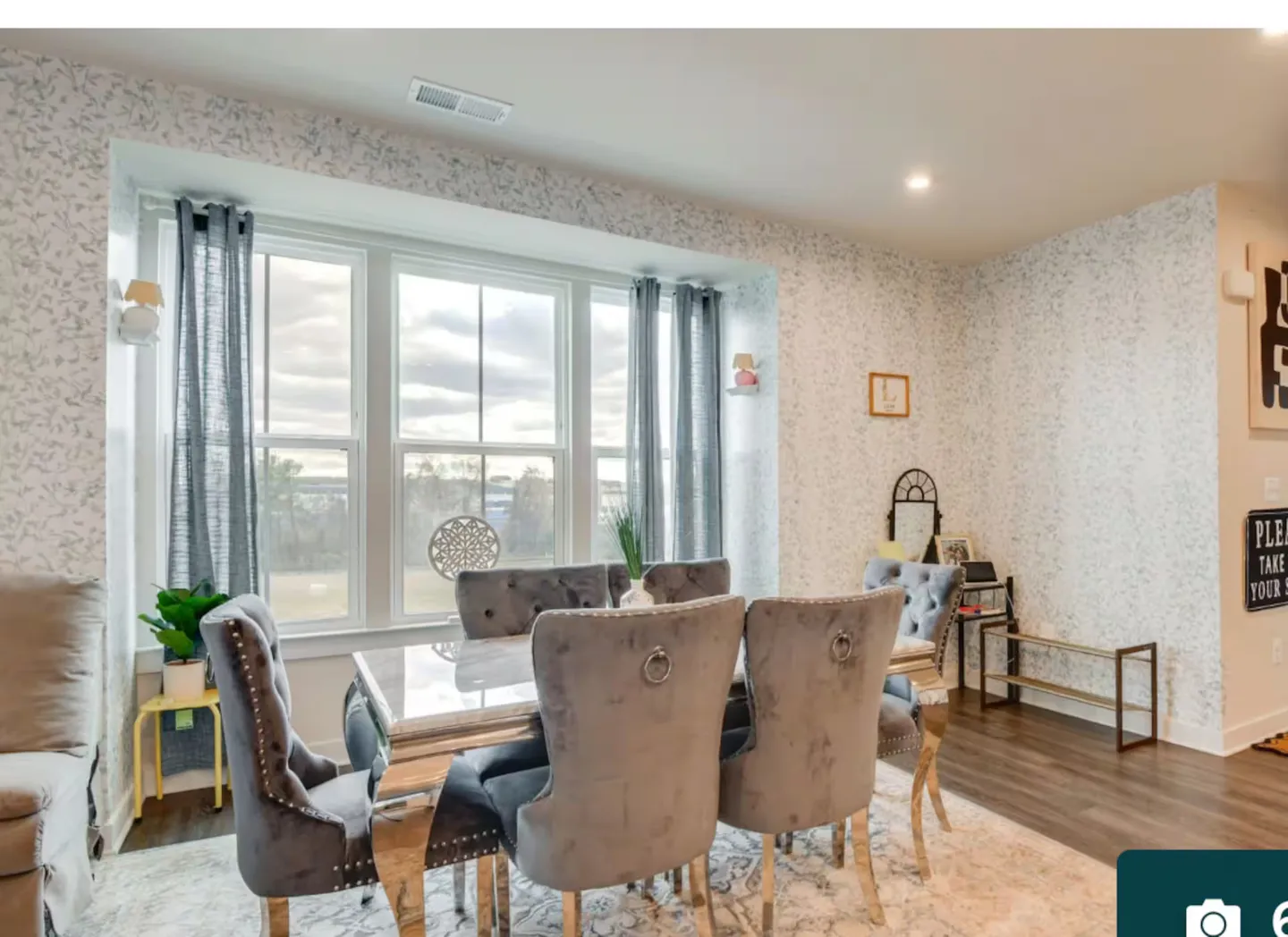 Dining area featuring a glossy dining table surrounded by upholstered gray chairs next to a large bay window.