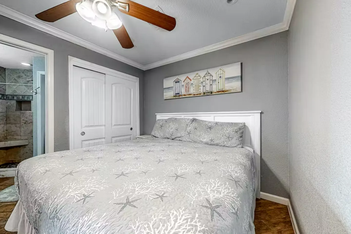 Bedroom featuring a made bed with starfish-patterned bedding, a ceiling fan, closet doors, and an open doorway to an en suite bathroom.