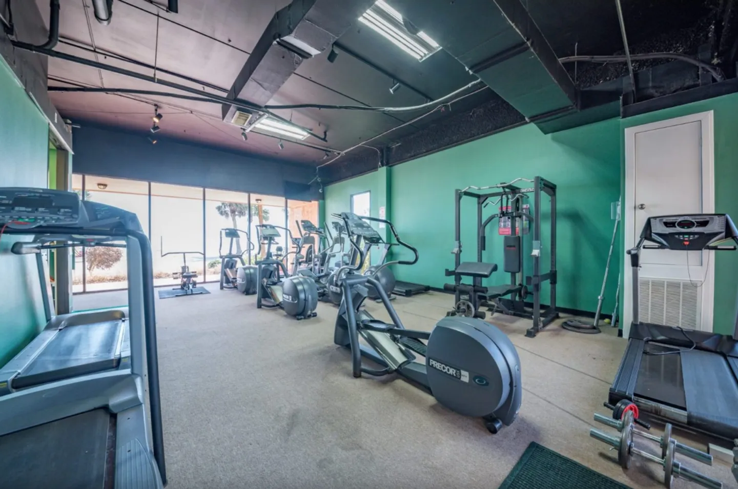 An indoor fitness room featuring treadmills, elliptical machines, exercise bikes, and a weight machine.