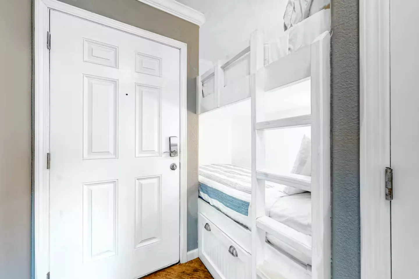 Built-in white bunk beds positioned next to a white interior door in an entryway or hallway.