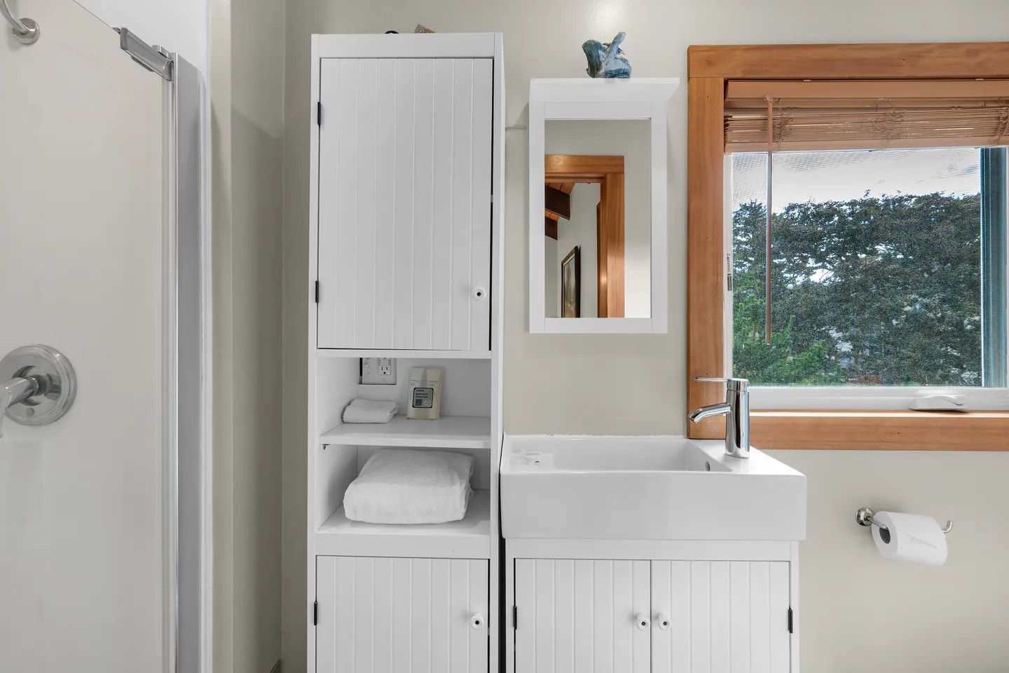 Bathroom with white vanity sink, tall white storage cabinet, medicine cabinet mirror, and a window framed in wood.