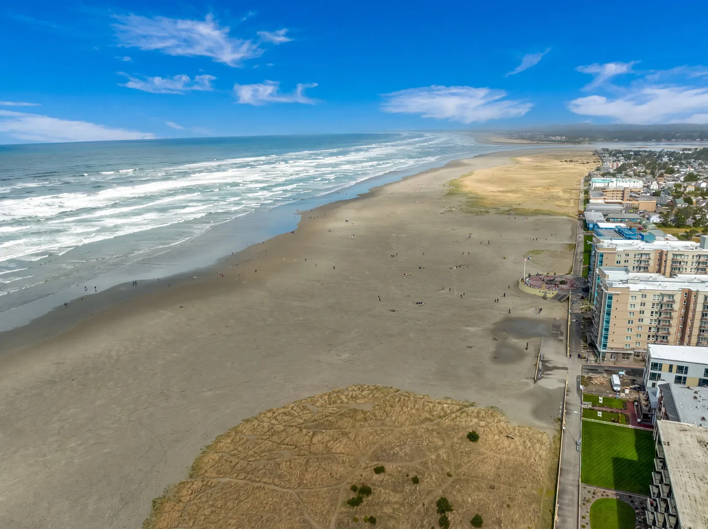 Aerial view of an expansive sandy beach and rolling ocean waves next to a coastal town promenade and buildings.
