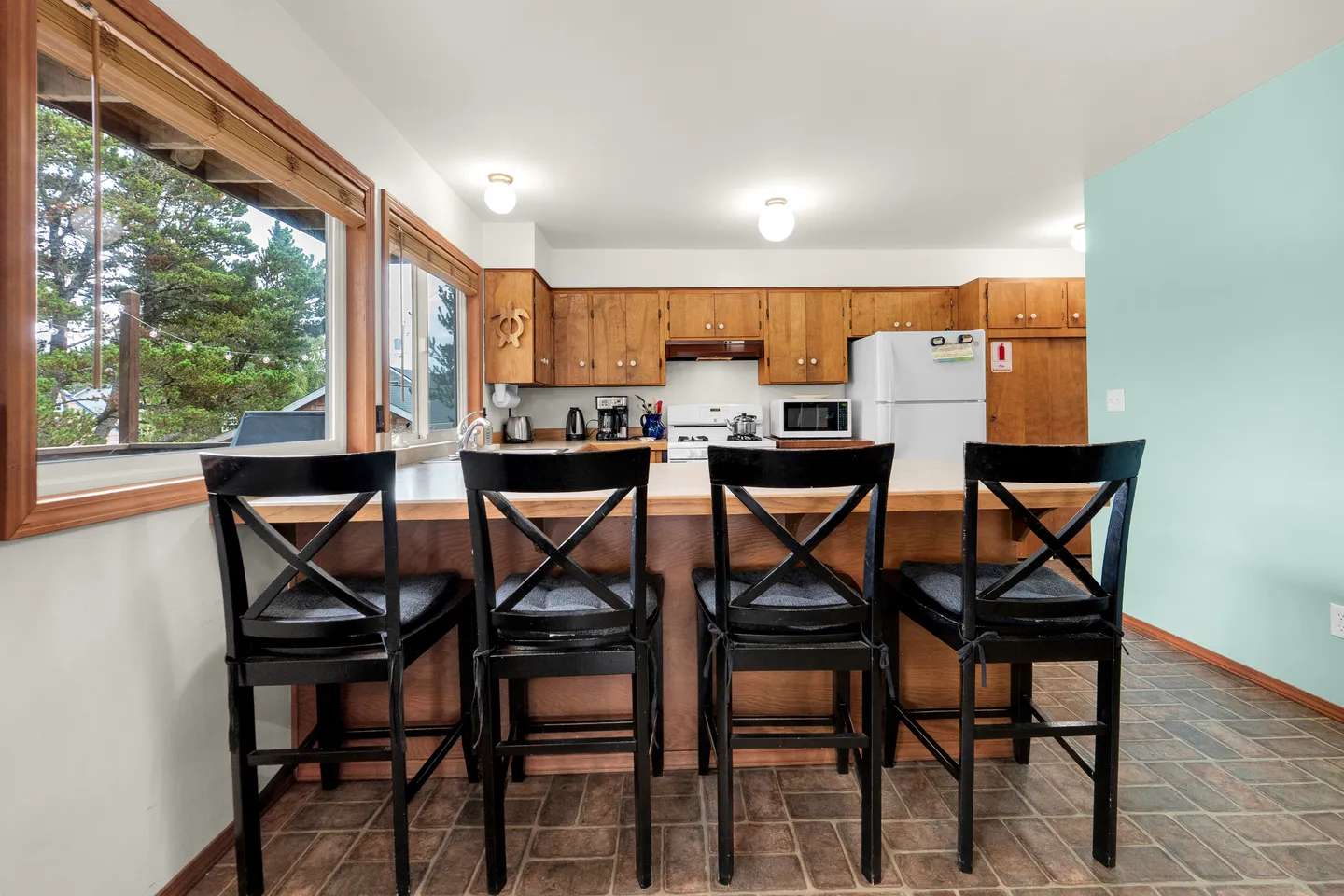 Kitchen with wooden cabinetry, white appliances, and a breakfast bar with four black wooden stools.