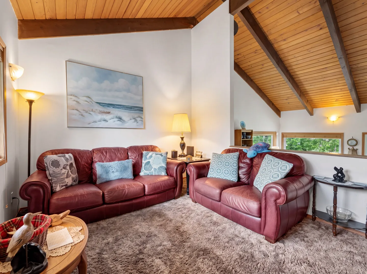 Living area featuring a burgundy leather sofa and loveseat beneath a vaulted wood-plank ceiling with exposed beams.