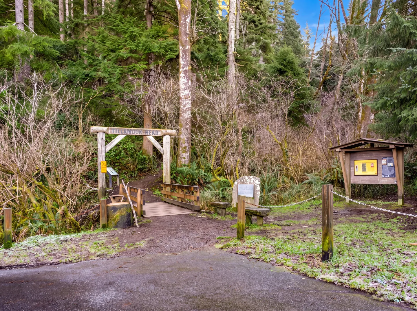 Trailhead entrance for Tillamook Head featuring a wooden archway, footbridge, and information kiosk bordering a dense forest.