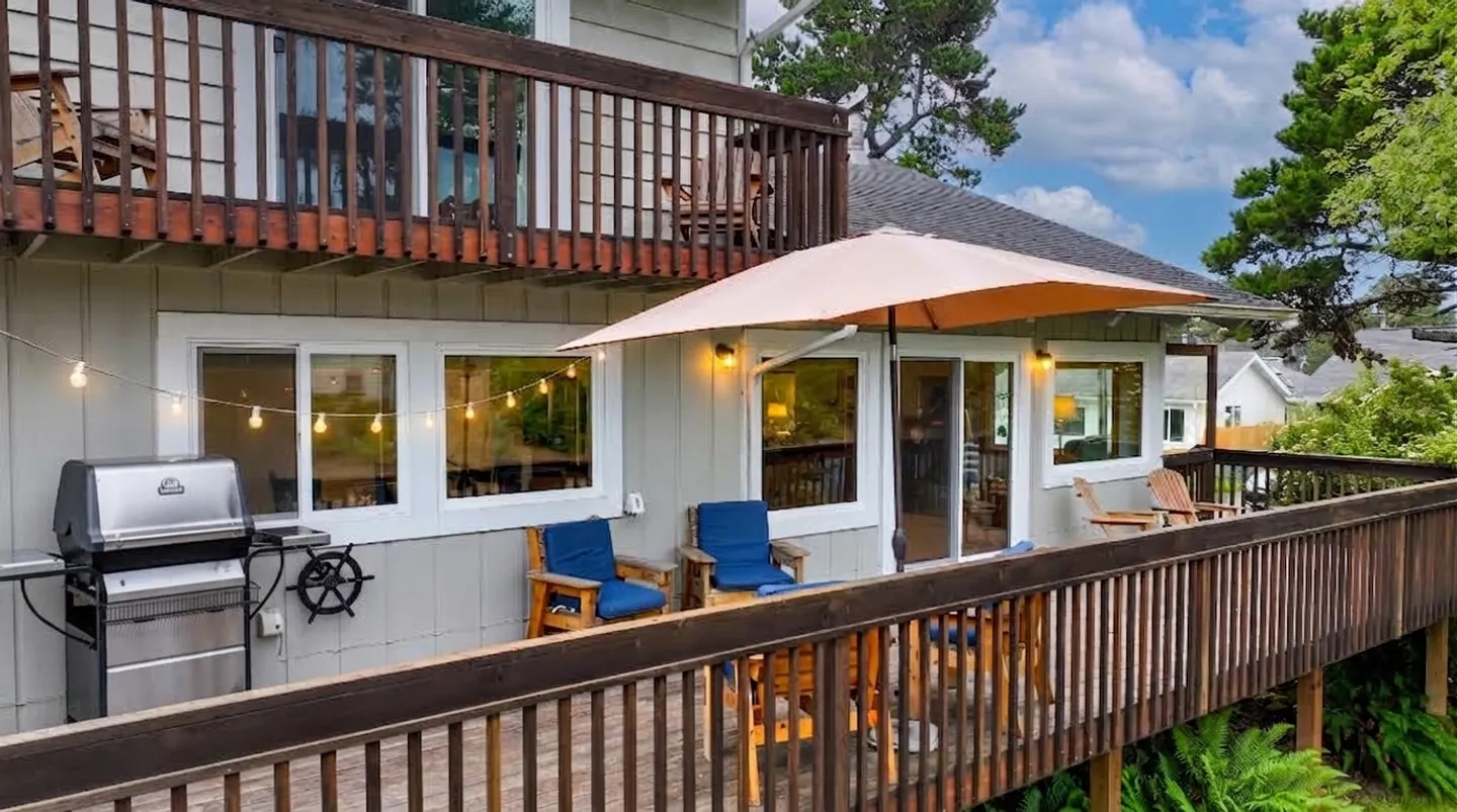 Outdoor elevated deck with outdoor seating, a patio umbrella, string lights, and a barbecue grill.