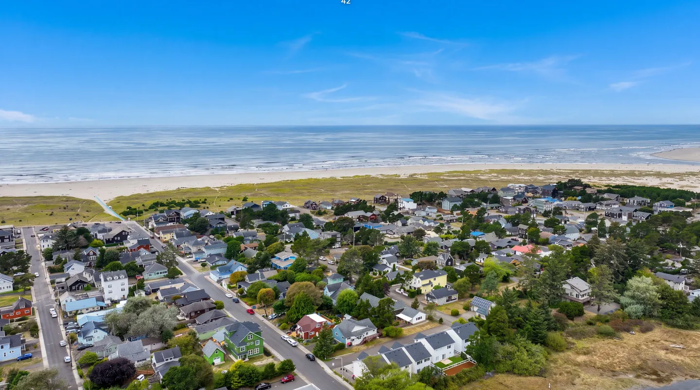 Aerial view of a coastal neighborhood with residential homes near a wide sandy beach and ocean under a blue sky.