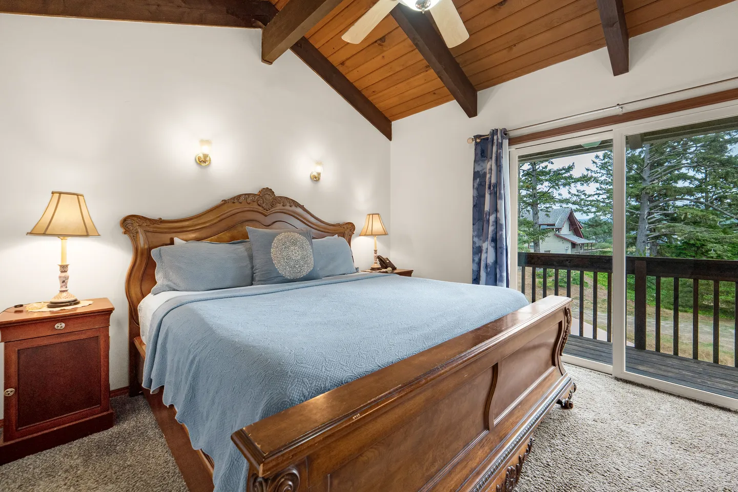 Bedroom with a wood sleigh bed, vaulted wood-paneled ceiling with exposed beams, and sliding glass doors to a balcony.