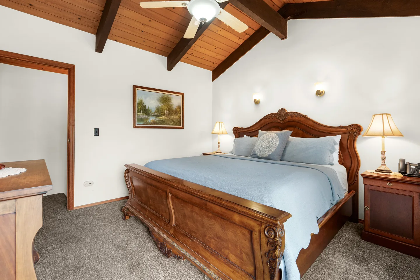Bedroom with a large wooden sleigh bed, carpeted floor, and a vaulted wood-paneled ceiling with dark beams.