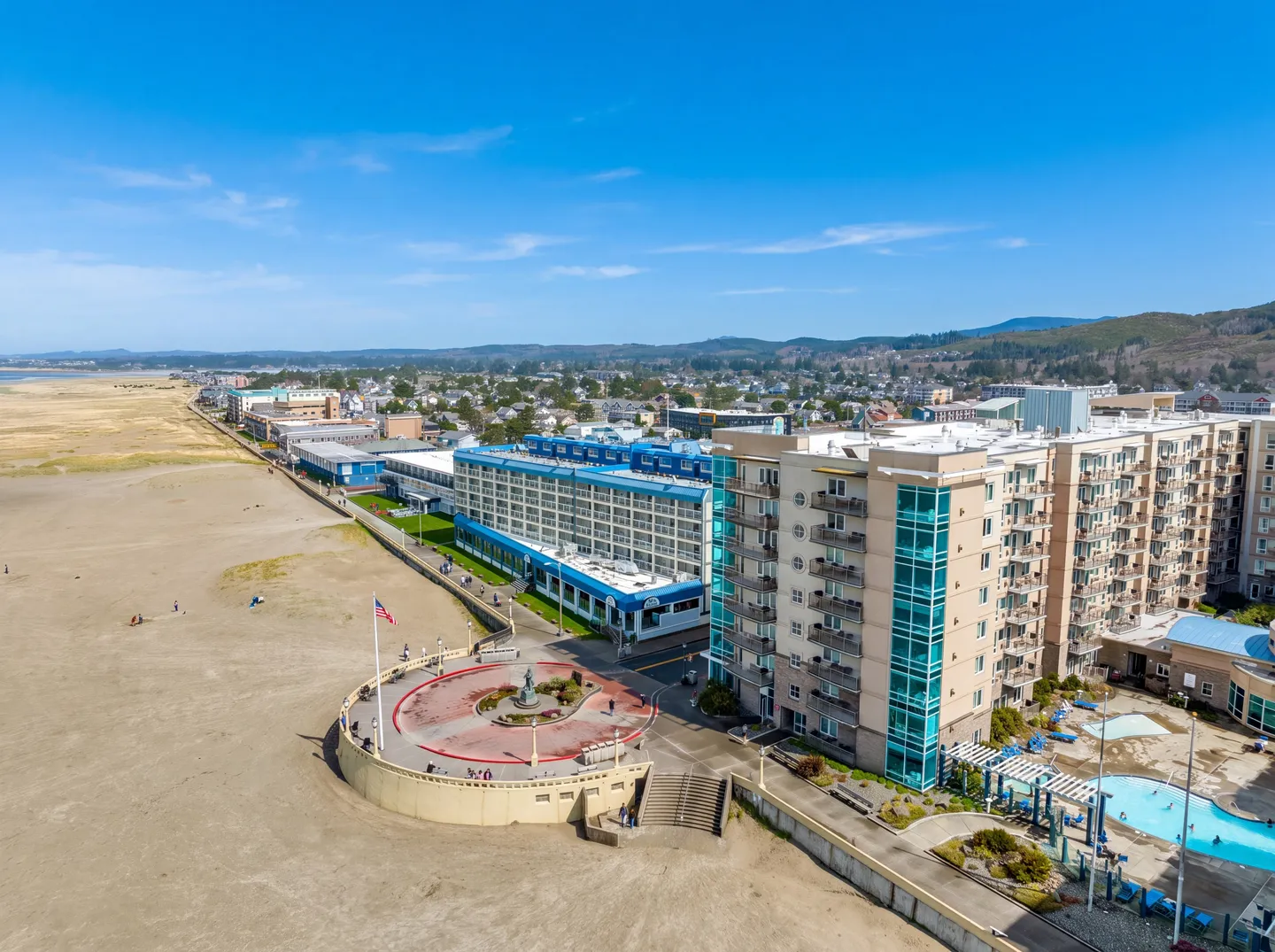 Aerial view of a coastal resort building adjacent to a sandy beach and circular promenade turnaround.