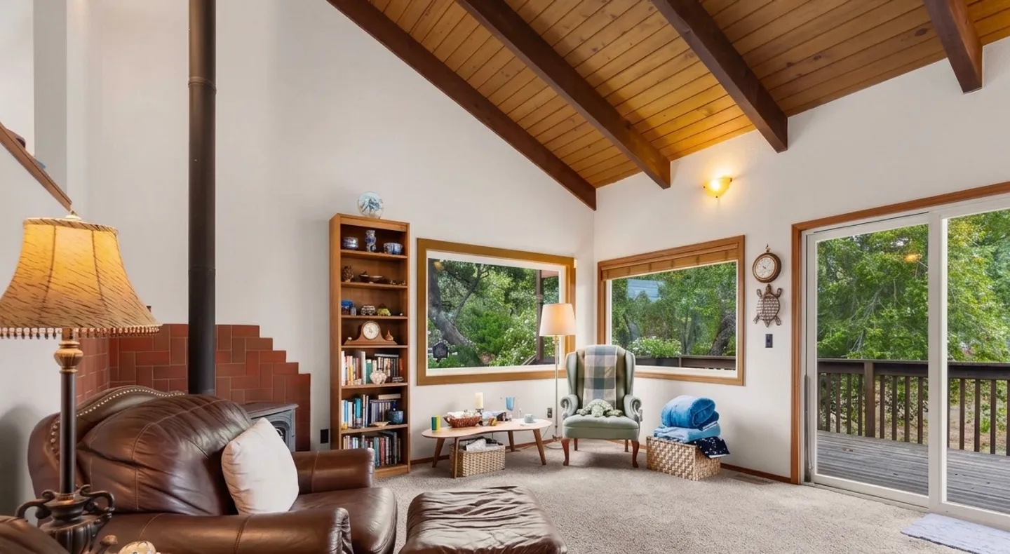 Living room with vaulted wood-beamed ceiling, leather armchair, wood stove, and sliding glass door leading to a deck.