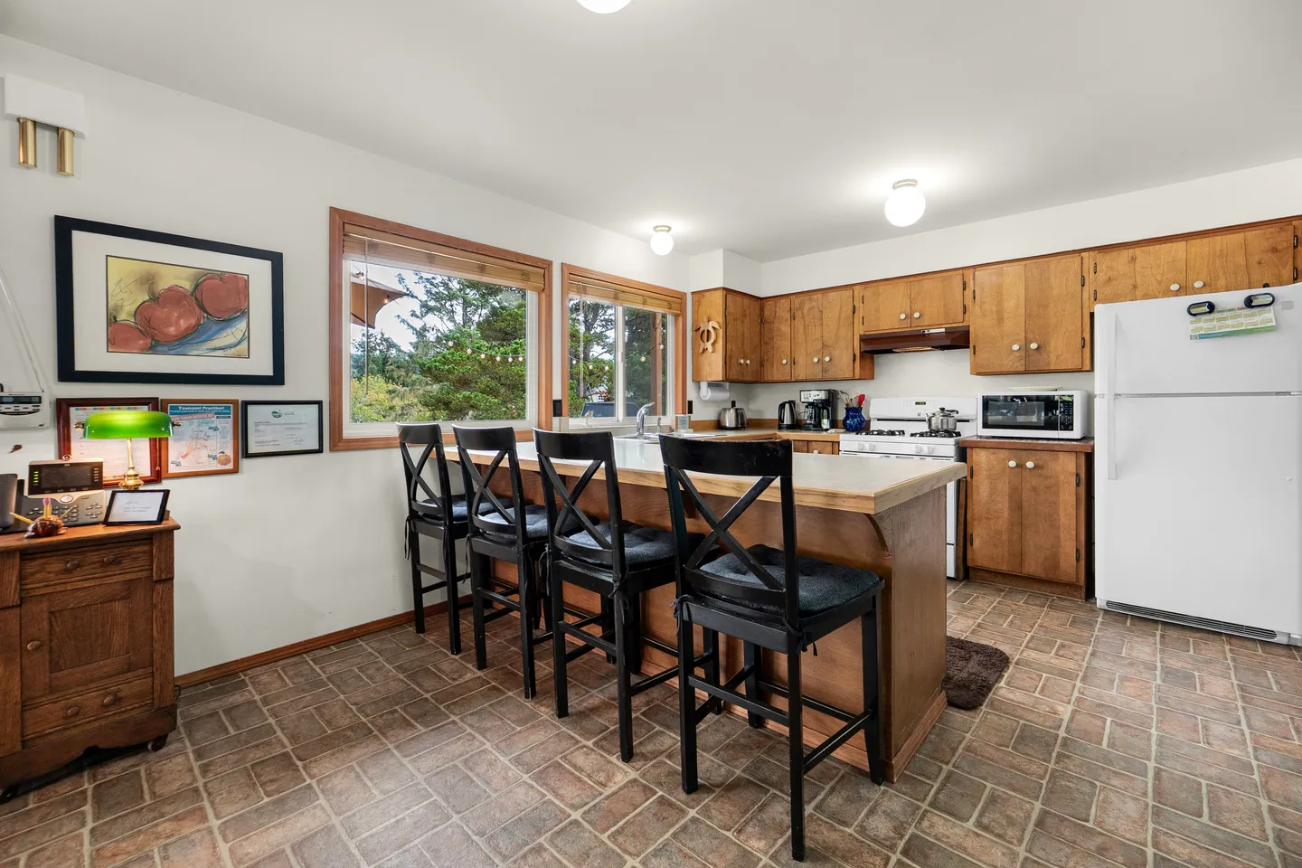 Kitchen featuring a central island with four black barstools, wood cabinetry, white appliances, and tiled flooring.