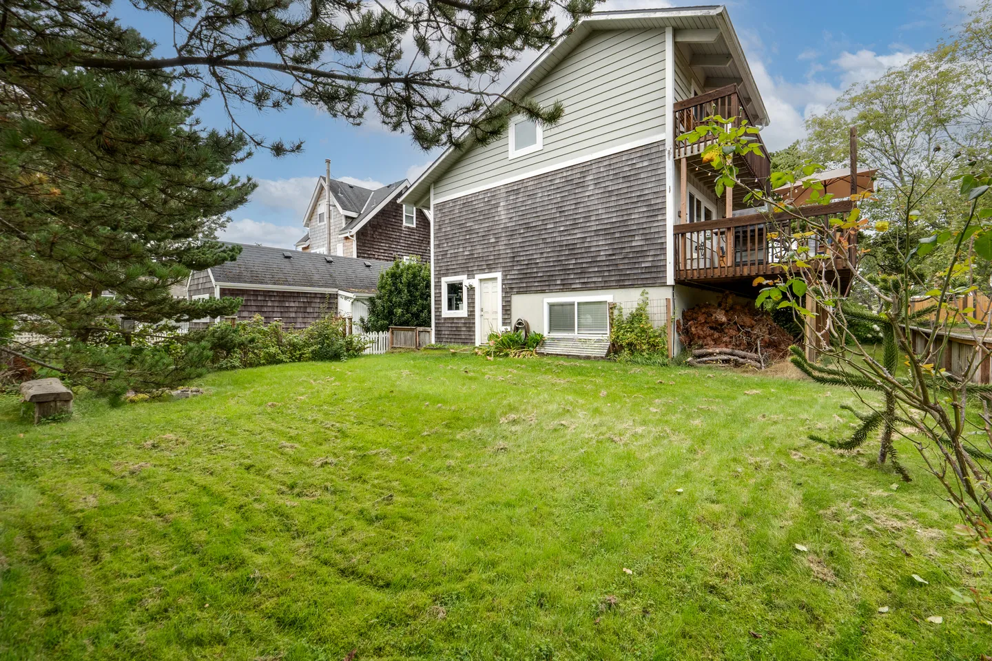 Rear exterior view of a multi-story home featuring wood shingle and light siding, an upper deck, and a grassy backyard framed by trees.