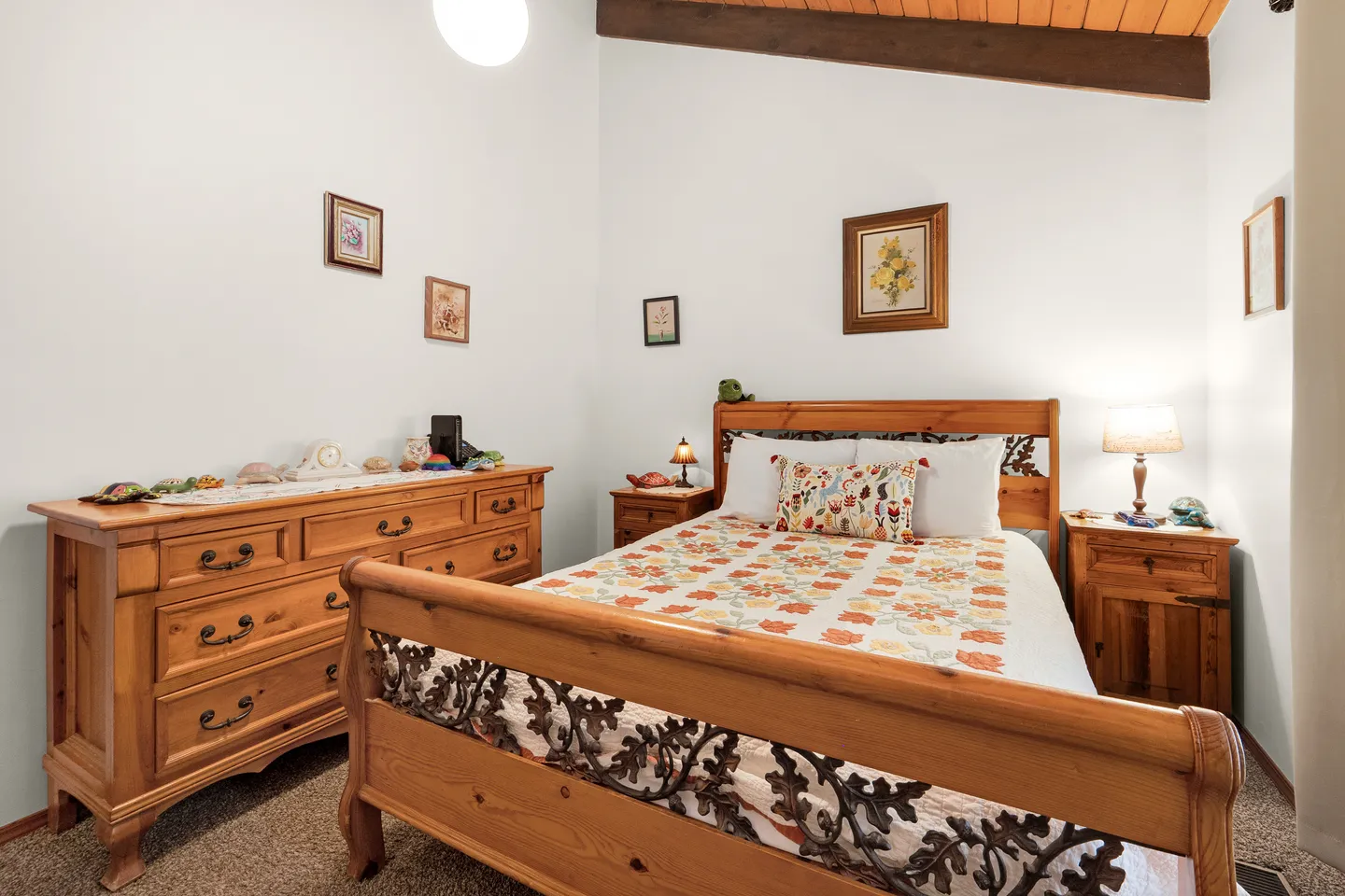 Bedroom featuring a wooden bed frame with iron scrollwork, a floral quilt, matching wooden dresser, and two nightstands with lamps.
