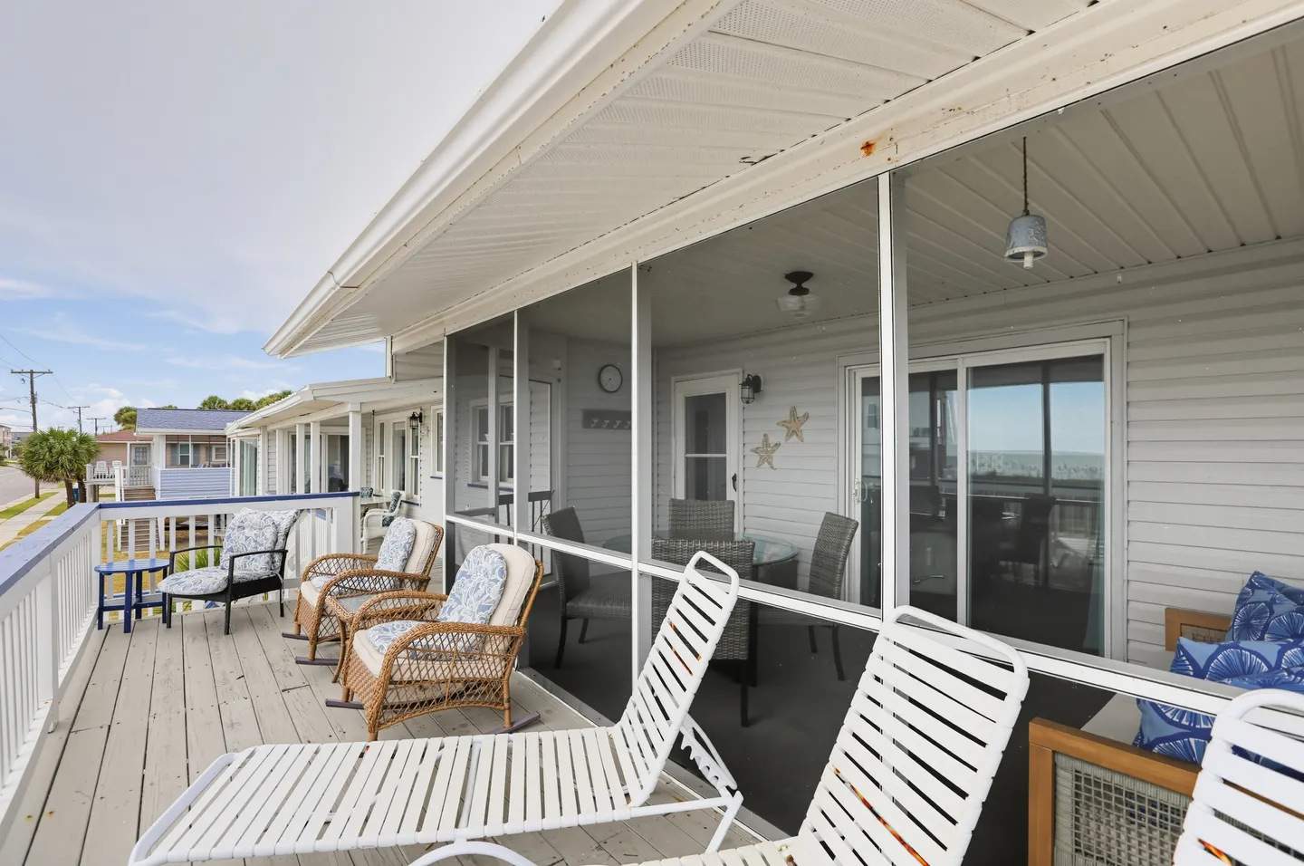 Outdoor deck and adjacent screened porch area with wicker armchairs, lounge chairs, and dining furniture.