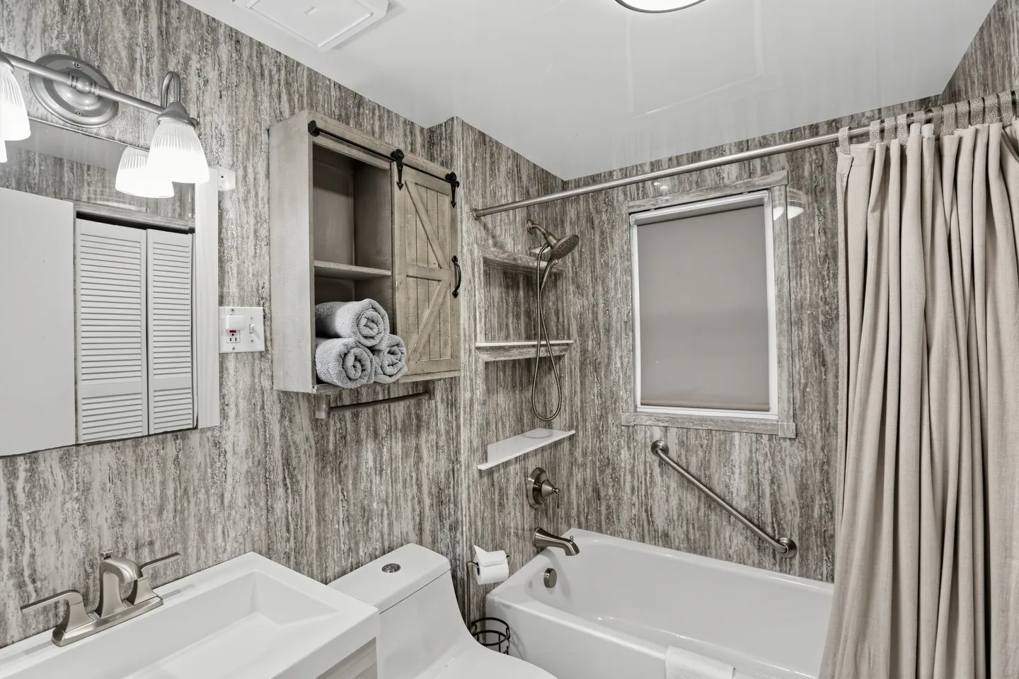 Bathroom with textured gray wall panels, a white bathtub and shower combination, a toilet, and a vanity sink.