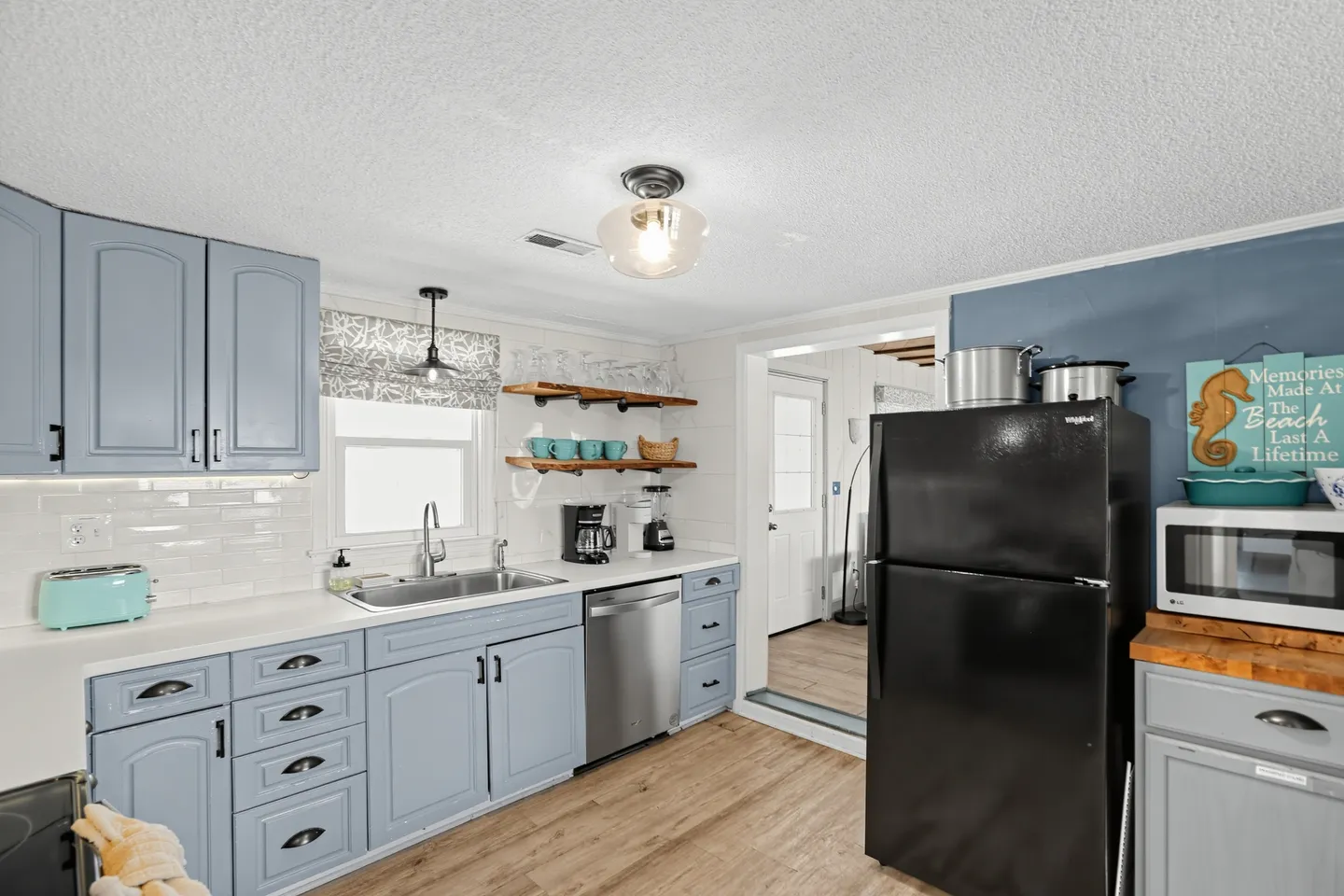 Kitchen with light blue cabinetry, white countertops, black refrigerator, stainless steel dishwasher, and open shelving.