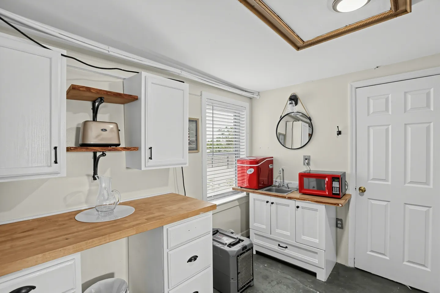 Kitchenette area with white cabinets, wood countertops, a small sink, red microwave, and red mini cooler.