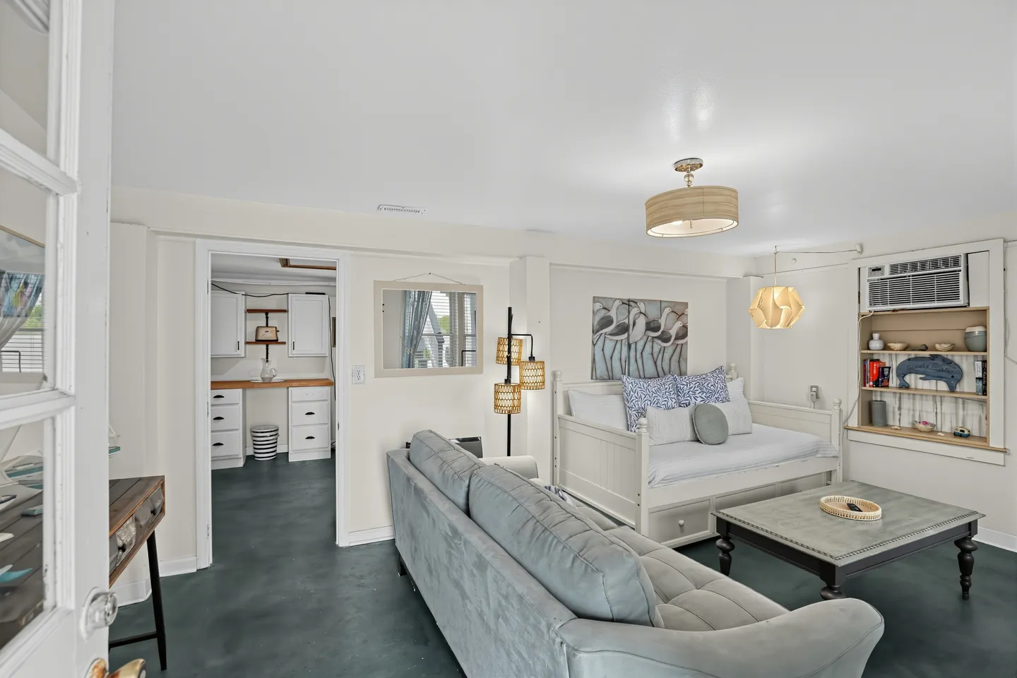 Living room with gray sofa, coffee table, daybed with trundle, and an open doorway leading to a workspace area.