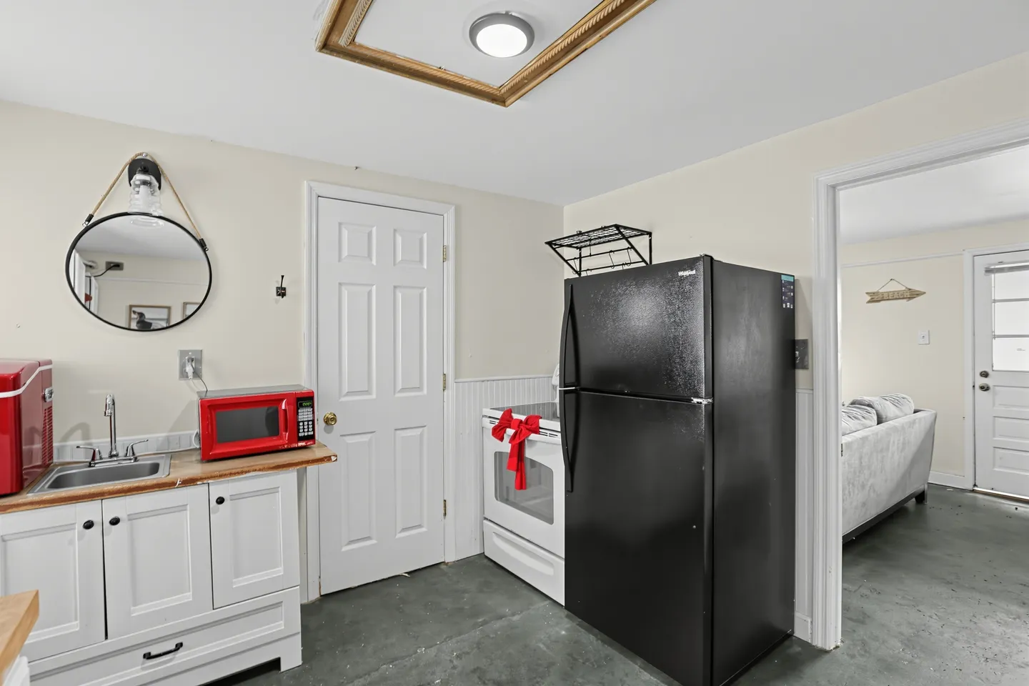 Kitchenette featuring a white sink cabinet with butcher block counters, a red microwave, a black refrigerator, and a white oven with a red bow.