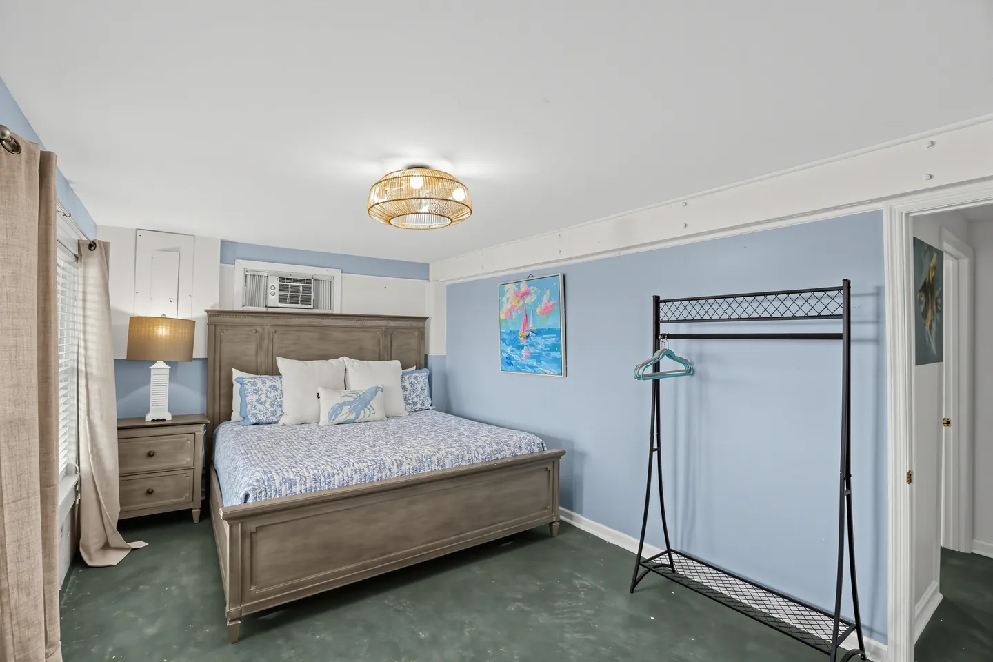 Bedroom with light blue walls, a dark wood-framed bed with blue and white bedding, a metal garment rack, and a bedside nightstand with a lamp.