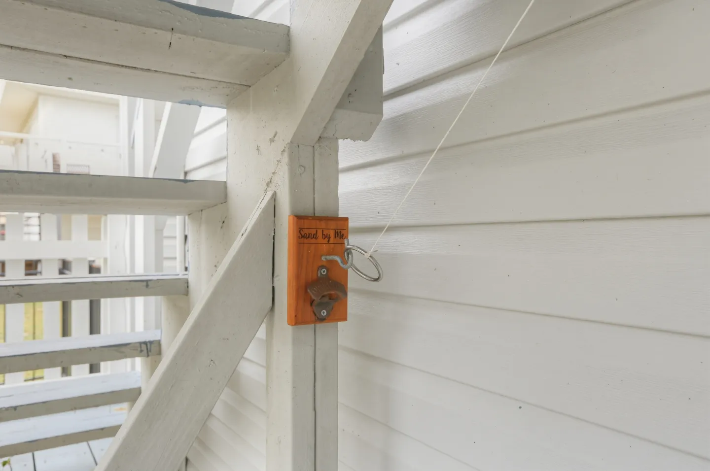 Close-up of a wall-mounted hook-and-ring game and bottle opener on a wooden post beside outdoor stairs.