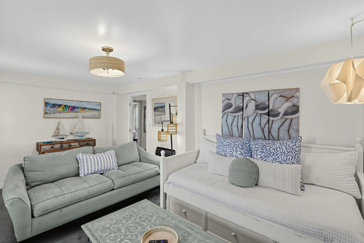 Living area with a light green sofa, a white daybed, a patterned coffee table, and coastal-themed wall art.