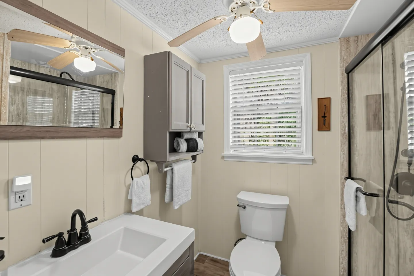 Bathroom with white toilet, vanity with rectangular sink, ceiling fan, and sliding glass shower doors.