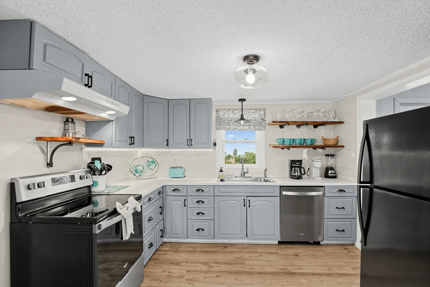 A kitchen with light blue cabinets, white countertops, wood-style flooring, a black range stove, and a stainless steel dishwasher.