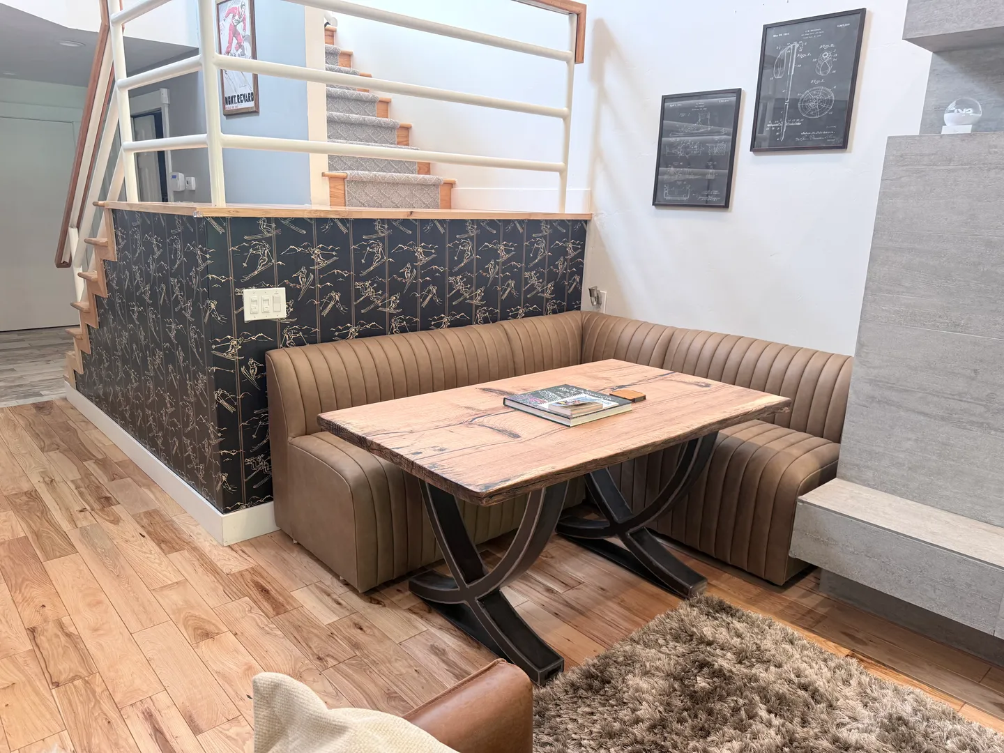 Dining banquette with an upholstered corner bench and wooden table situated near a staircase and fireplace.