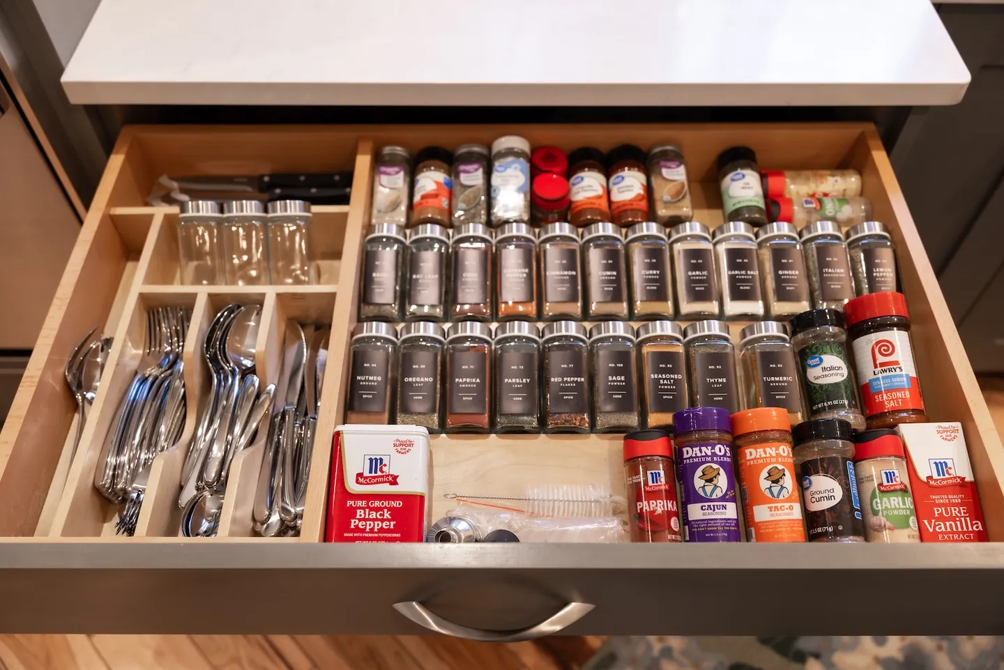 Open kitchen drawer organized with silverware, knives, and numerous spice containers.