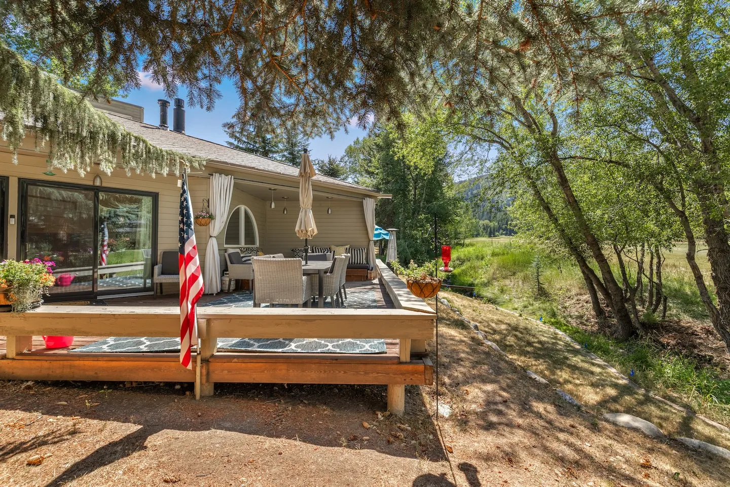 Outdoor wooden deck with patio dining furniture, shaded by trees and overlooking a grassy natural landscape.