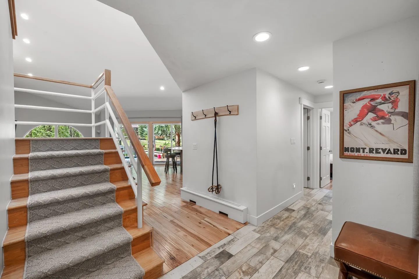 Entryway and hallway featuring carpeted stairs with a white and wood railing, wood and tile flooring, and a wall hook rack with ski poles.