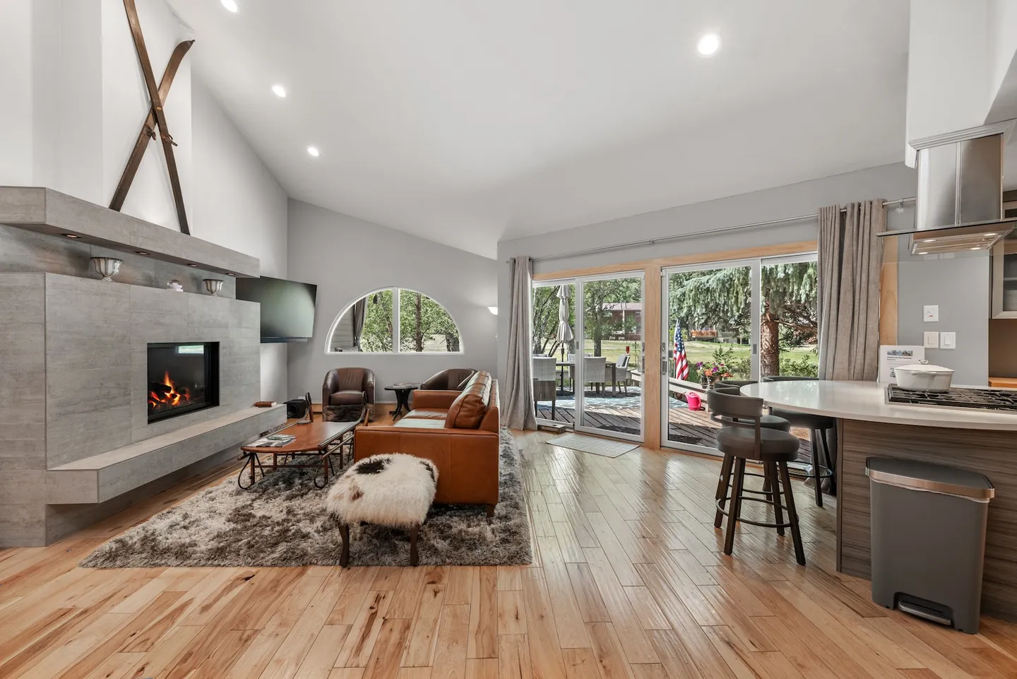 Open living area with vaulted ceilings, a modern tiled fireplace, leather couch, and sliding glass doors leading to an outdoor deck.